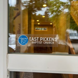 Clear Sticker 1 - Stickersandmore.com Sticker on a glass door reading 'East Pickens Baptist Church' with a blue circular logo to the left.